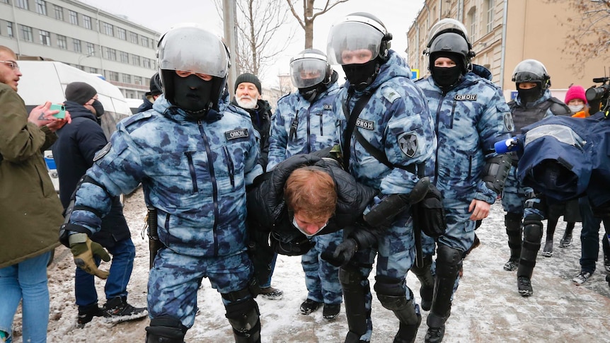 Four police officers in arctic camo carry a protester away. They are wearing heavy armor.