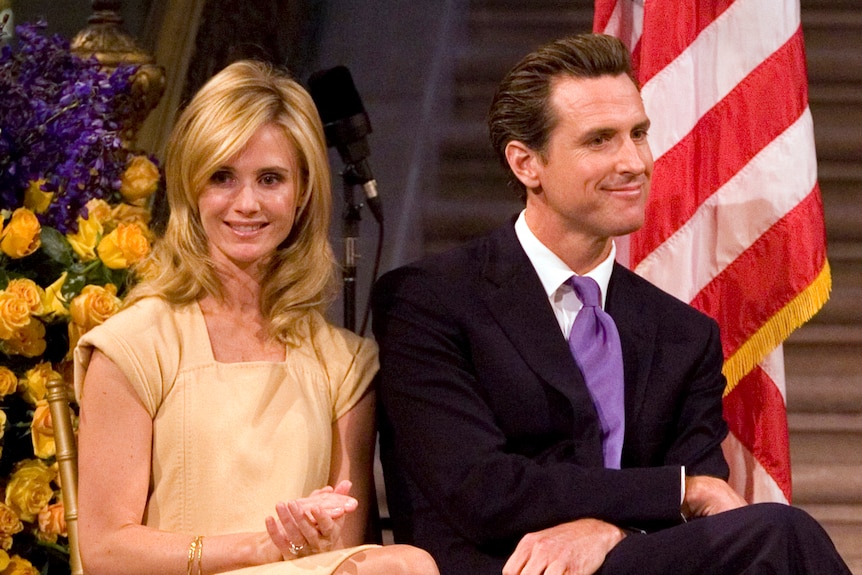 Gavin Newsom and Jennifer Siebel sit next to an American flag