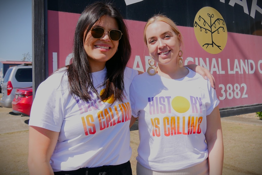 Young woman with dark hair and sunglasses, with another young woman with blonde hair, wearing white t-shirts