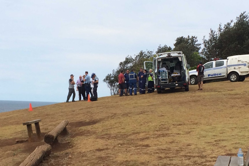 NSW ambulance workers and police talk on a hill near the sea