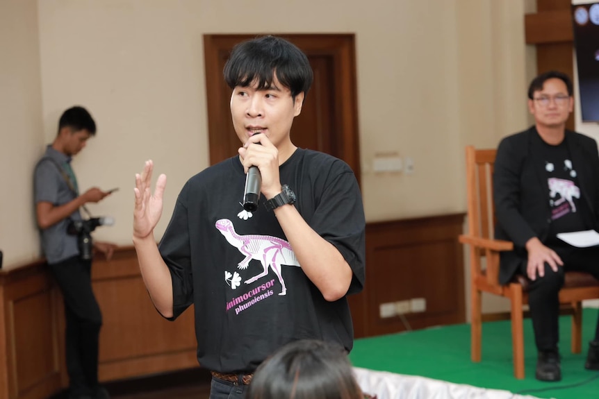 Sita Manitkoon speaks into a microphone, wearing a tshirt with a Minimocursor phunoiensis skeleton on it