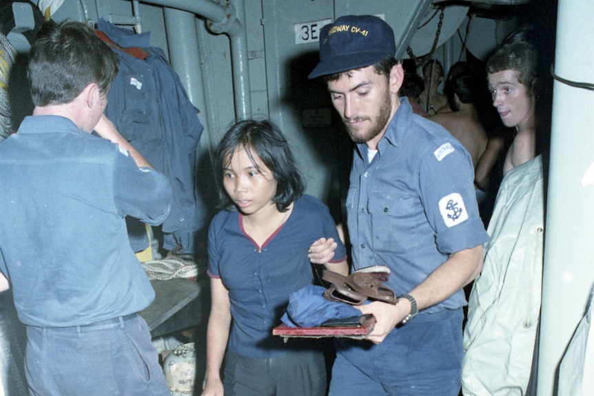 Two navy sailors help an Vietnamese girl on to the warship