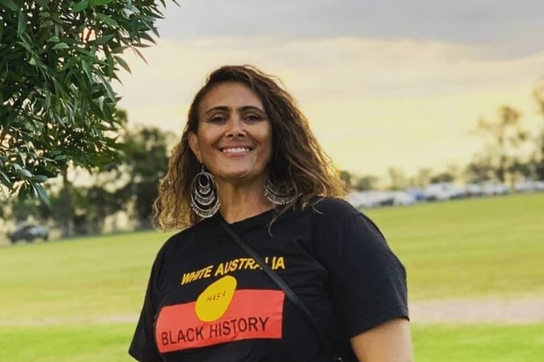 Woman stands in field wearing a tshirt with Indigenous flag on it 