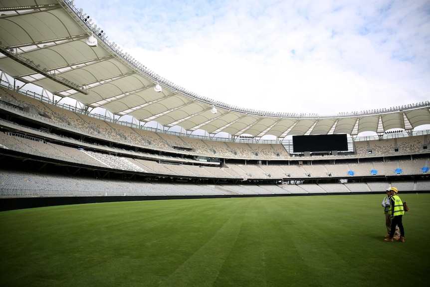 Two workmen stand inside the new stadium looking up to the stands.