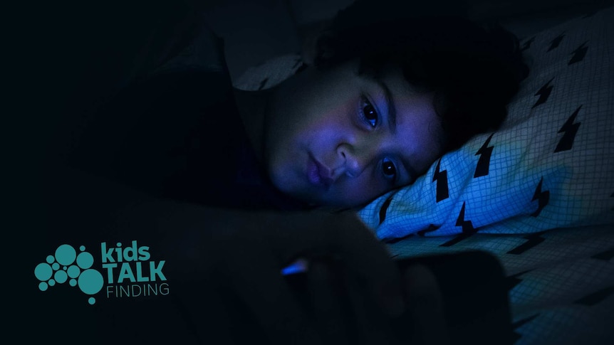 Boy lies in bed at night time looking into the screen of a phone. 'Kids Talk Finding' logo in the corner.