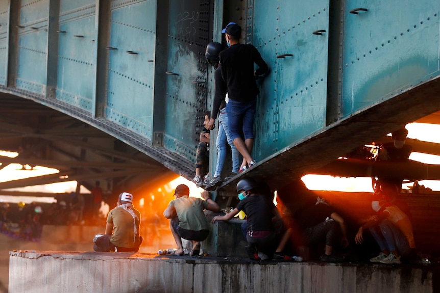 Protesters huddle under a green bridge as golden afternoon light streams through