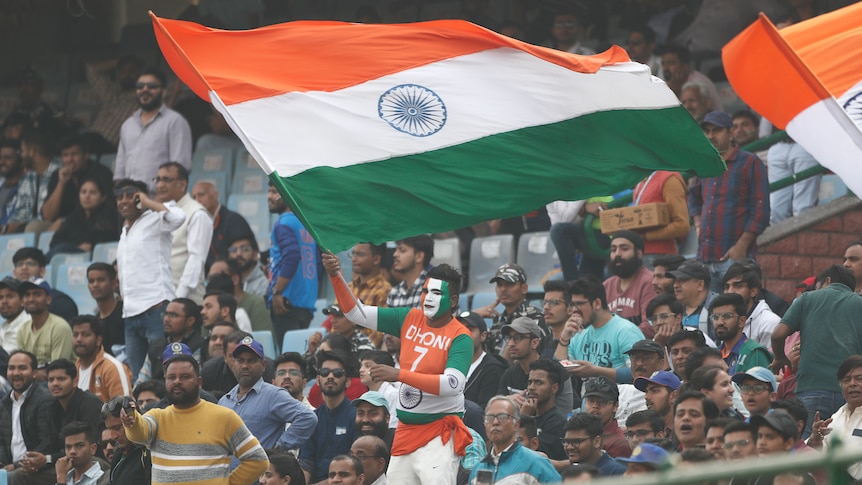 An Indian fan waves and Indian flag in the stands during a cricket test match.