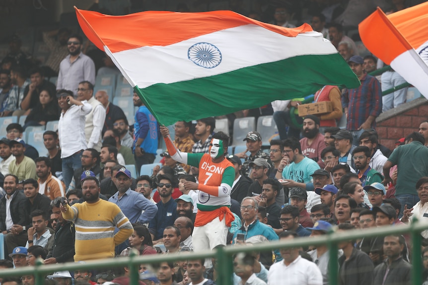 An Indian fan waves and Indian flag in the stands during a cricket test match.