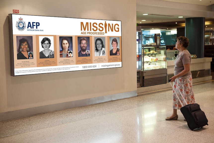 A woman stands and looks at a billboard showing faces of six missing people