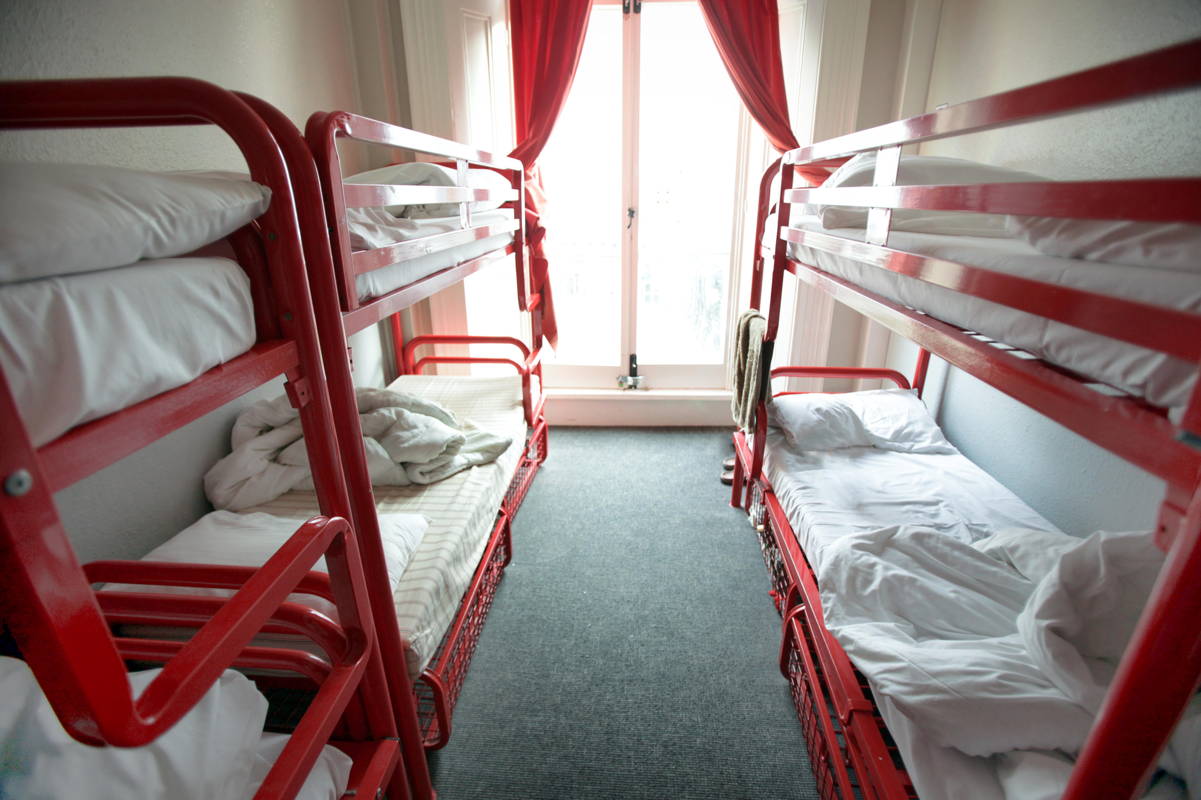 Bedroom with several red bunk beds and red curtains. Sun streams in the window