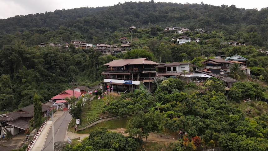 An aerial shot shows a village set on a lush green hill