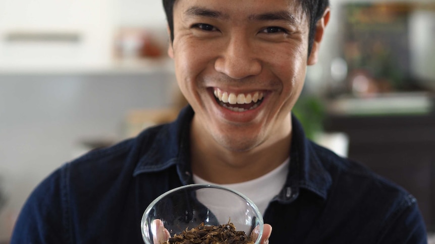 A grinning man holds a bowl of dried grasshoppers.