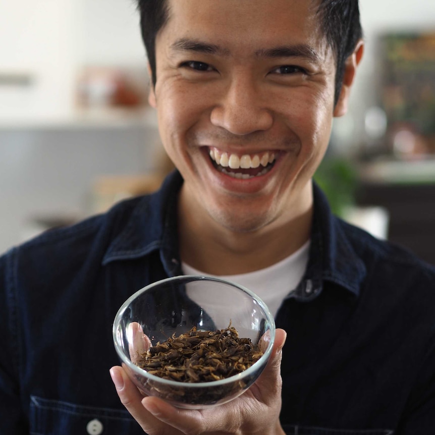 A grinning man holds a bowl of dried grasshoppers.