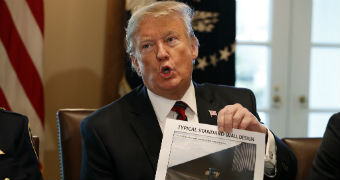 A man sitting at a desk hold up an image of a wall design that is printed on a piece of paper