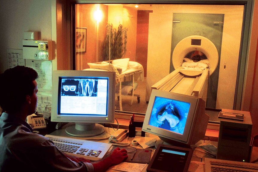 A patient lying in a medical scanner while a clinician looks at brain scan images