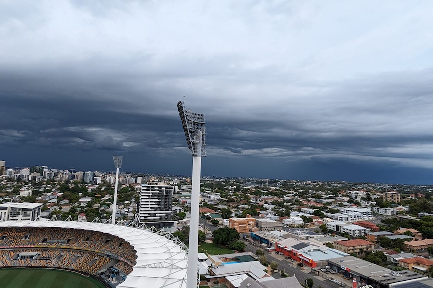 Storm clouds fill the skies above Brisbane, a stadium can be seen overlooking a city sprawl.
