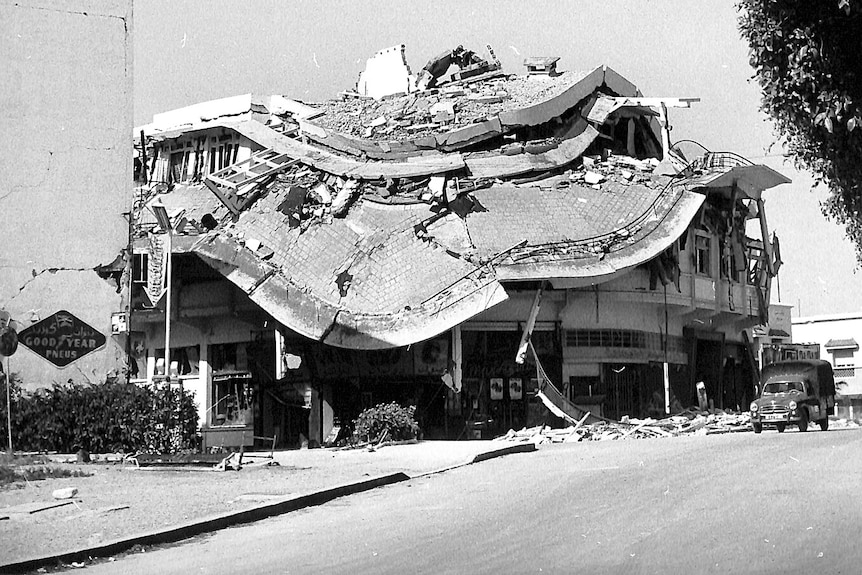 A black and white image shows a crumpled building. 