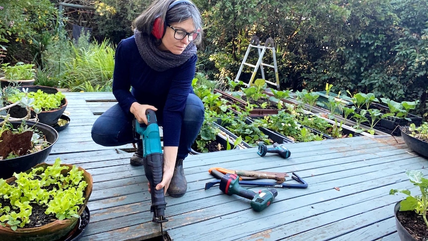 Katherine Wilson squats on the wooden deck of a house in a story about the many benefits of DIY projects.