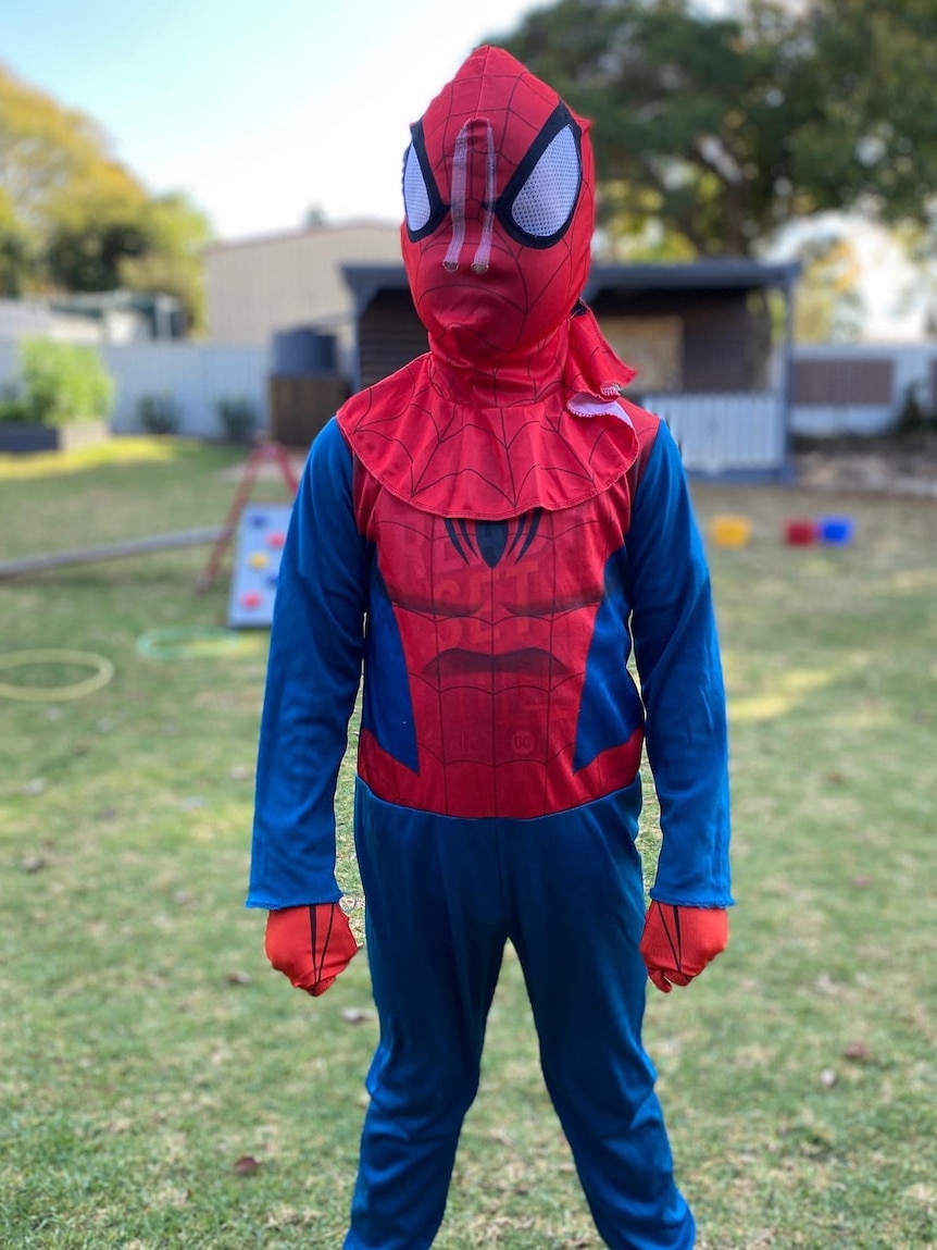 A little boy dressed in a Spider-Man outfit, standing in a yard.