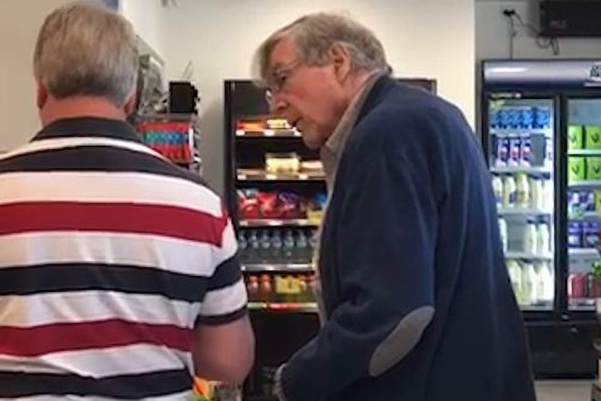 George Pell talks to a man while waiting in line at a petrol station
