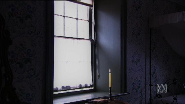 A candle burns beside a window