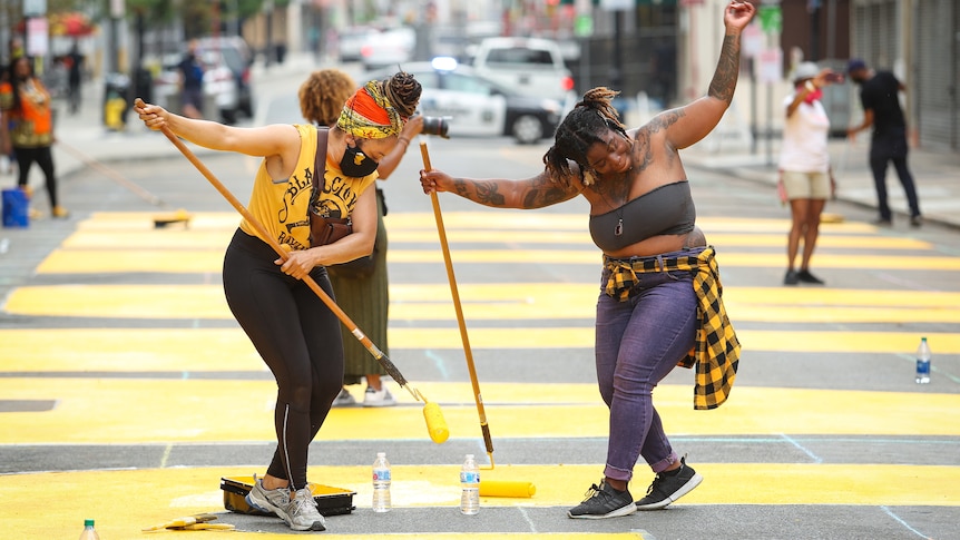 Two women dance while painting the words 'black lives matter' on road