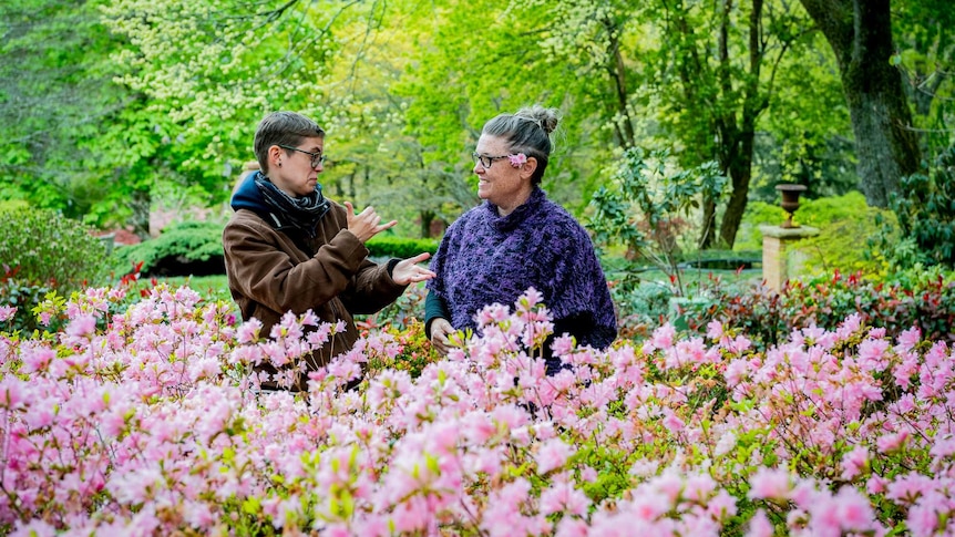 A man doing sign language to an older woman with flowers in the foreground