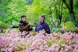 A man doing sign language to an older woman with flowers in the foreground