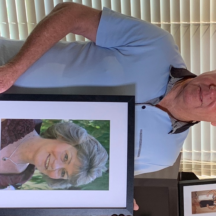 Tim Murphy holding up a frame with a photo of his deceased wife Delphine Murphy