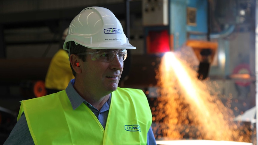 Mark McGowan wearing a hard hat in front of machinery.