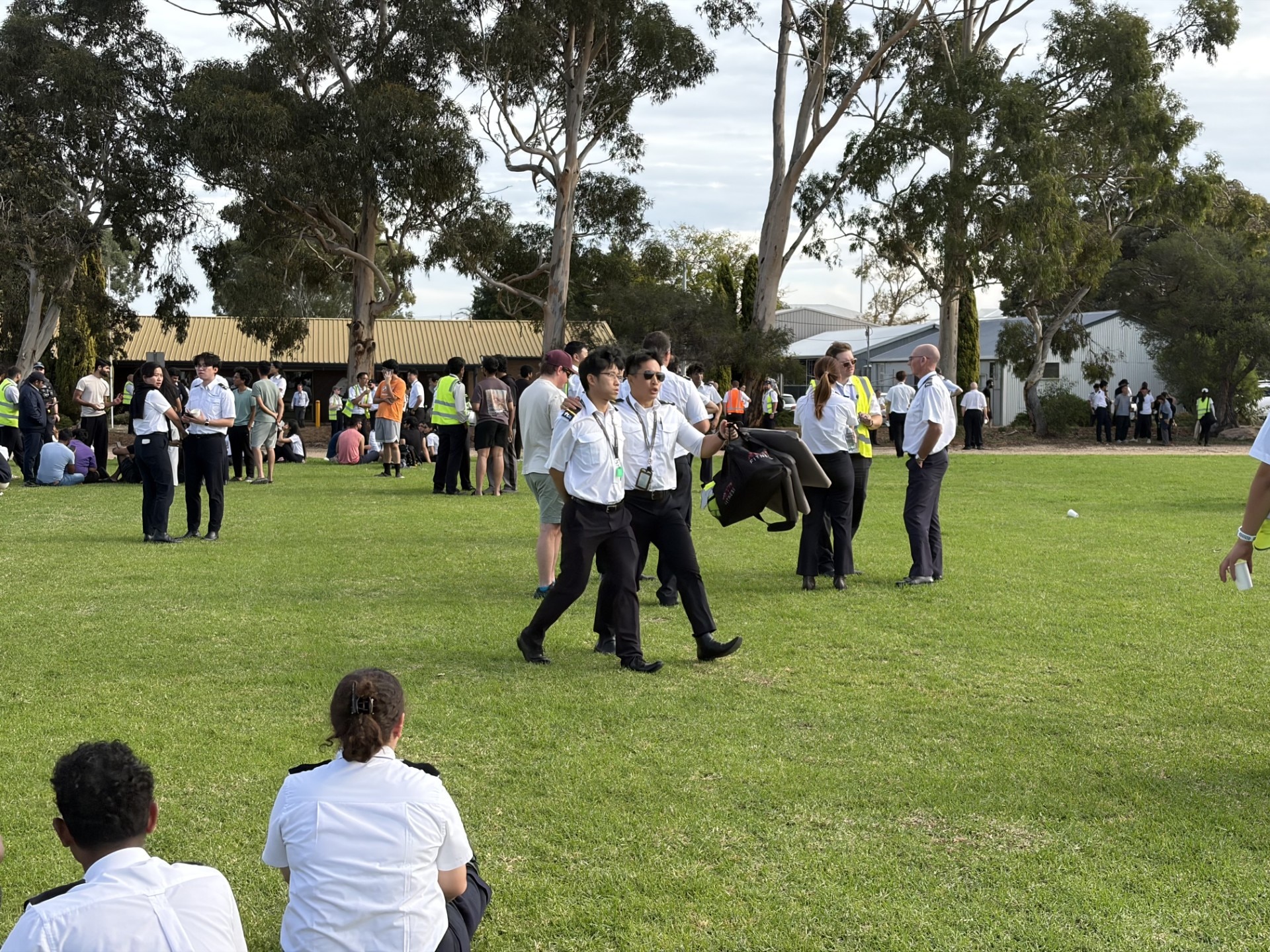 People, most in white shirts, mill around on a lawn.