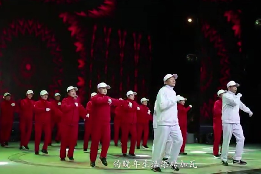 Older people in red and white tracksuits performance a dance.