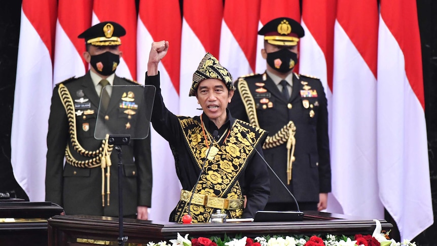 Indonesian President Joko Widodo, center, dressed in a traditional outfit, raises his fist as he delivers a speech.