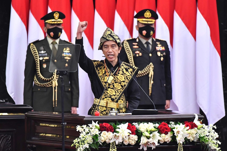 Indonesian President Joko Widodo, center, dressed in a traditional outfit, raises his fist as he delivers a speech.