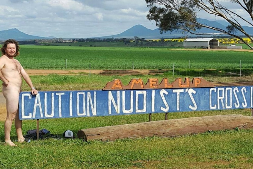 A photo of Willy Steel in front of the Caution Nudist's Crossing sign