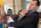 A man in a suit punches an older man in a suit.