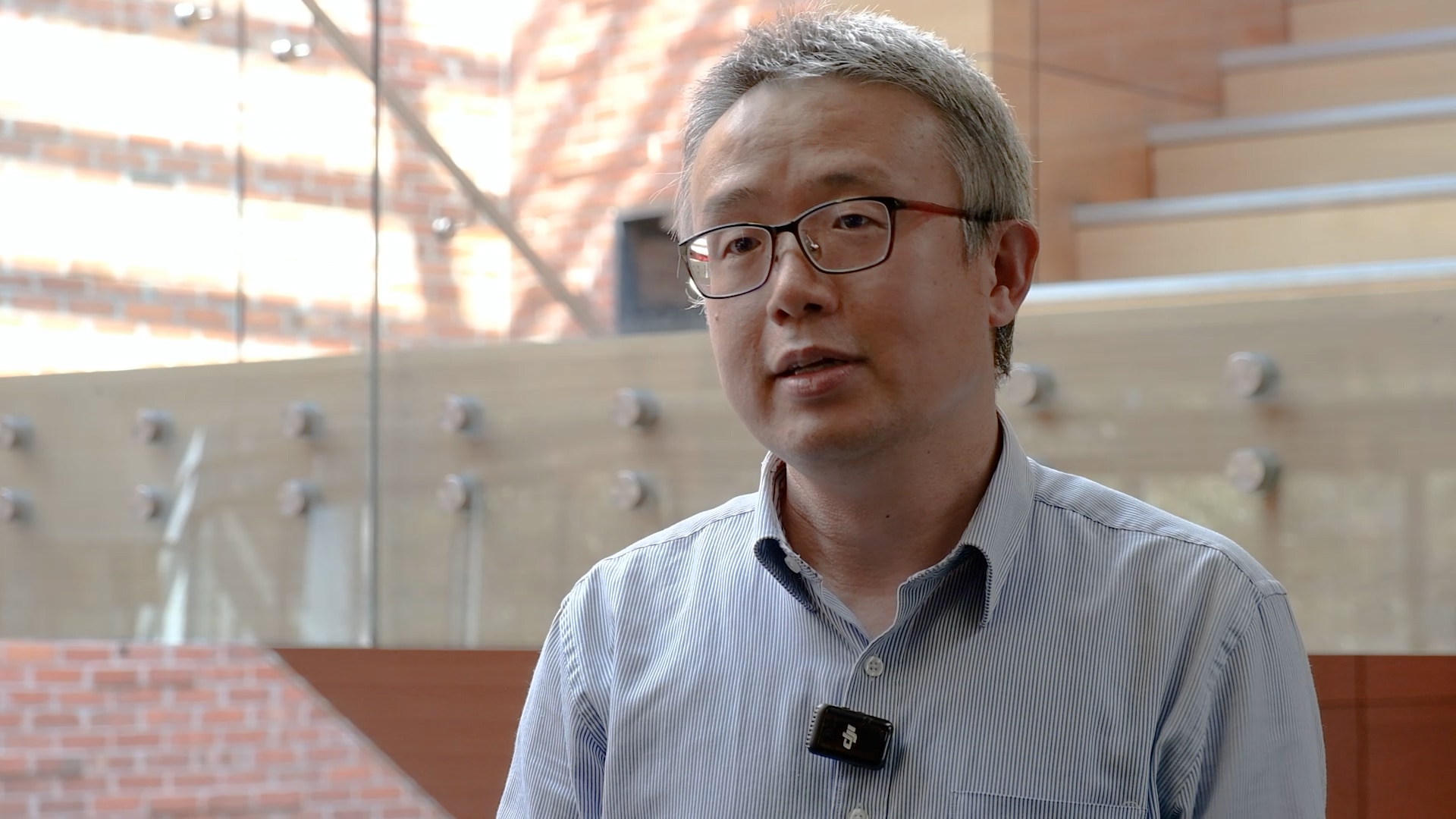 A grey-haired man in glasses in a large building.
