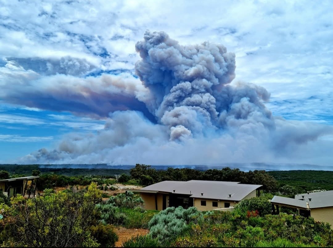 Una foto del paisaje del suroeste con una casa en primer plano y una enorme nube de humo al fondo.