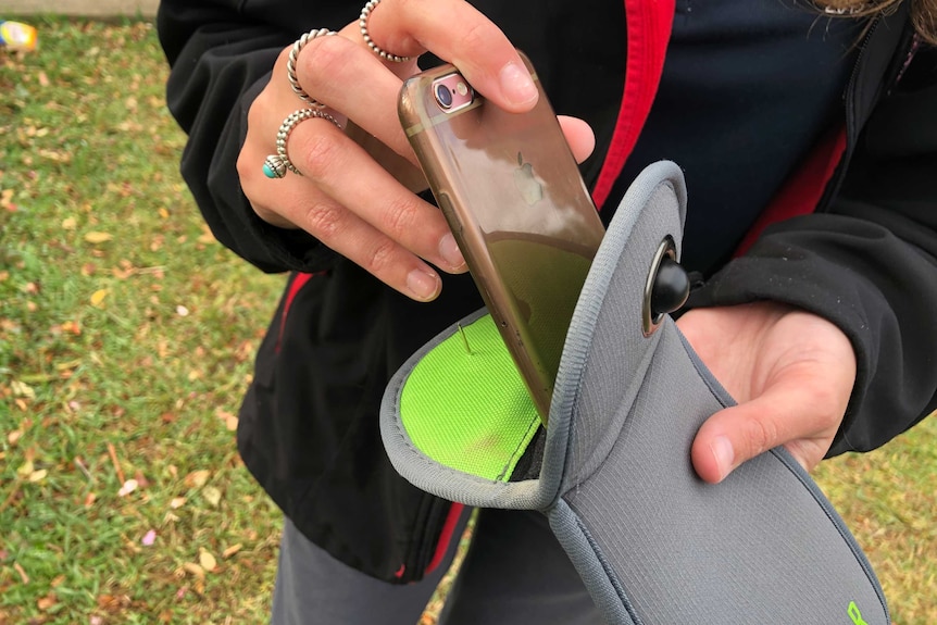 A close-up of a hand placing a mobile phone into a pouch