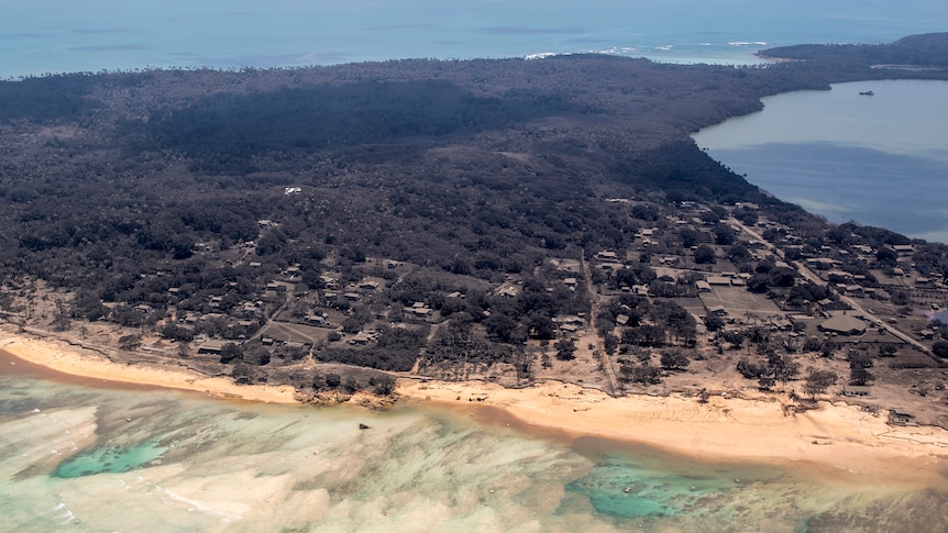 Volcanic ash covers roof tops and vegetation on an island as seen from an aerial view.