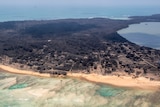 Volcanic ash covers roof tops and vegetation on an island as seen from an aerial view.