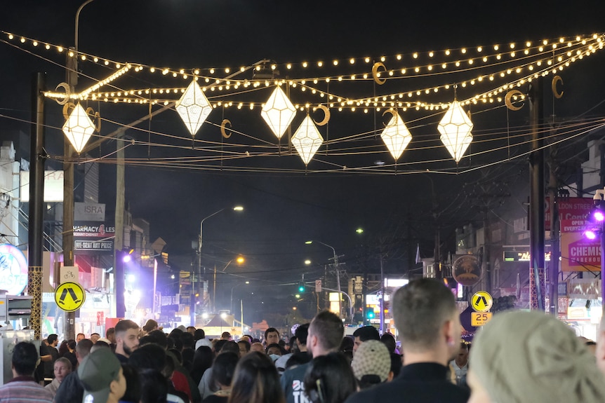 A veiw of lanterns stung over a busy crowd walking on a street in Lakemba during Ramadan.