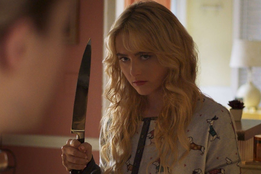 A scene from the movie Freaky with Kathryn Newton, a teen girl, in the foreground and a menacing killer in the background