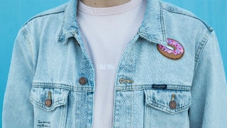 Close up of man wearing shirt and denim jacket standing by a blue wall