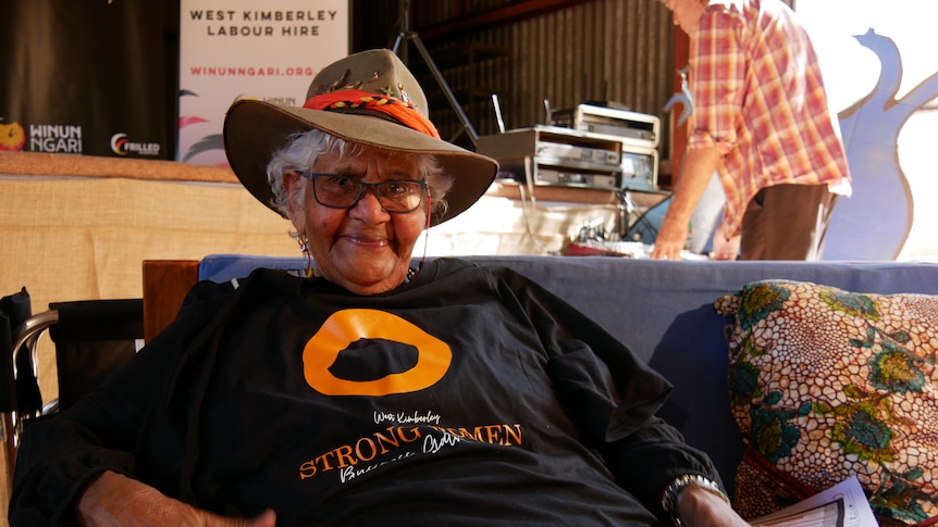 A happy smiling Indigenous woman in a cowboy hat, with a black and orange event shirt 