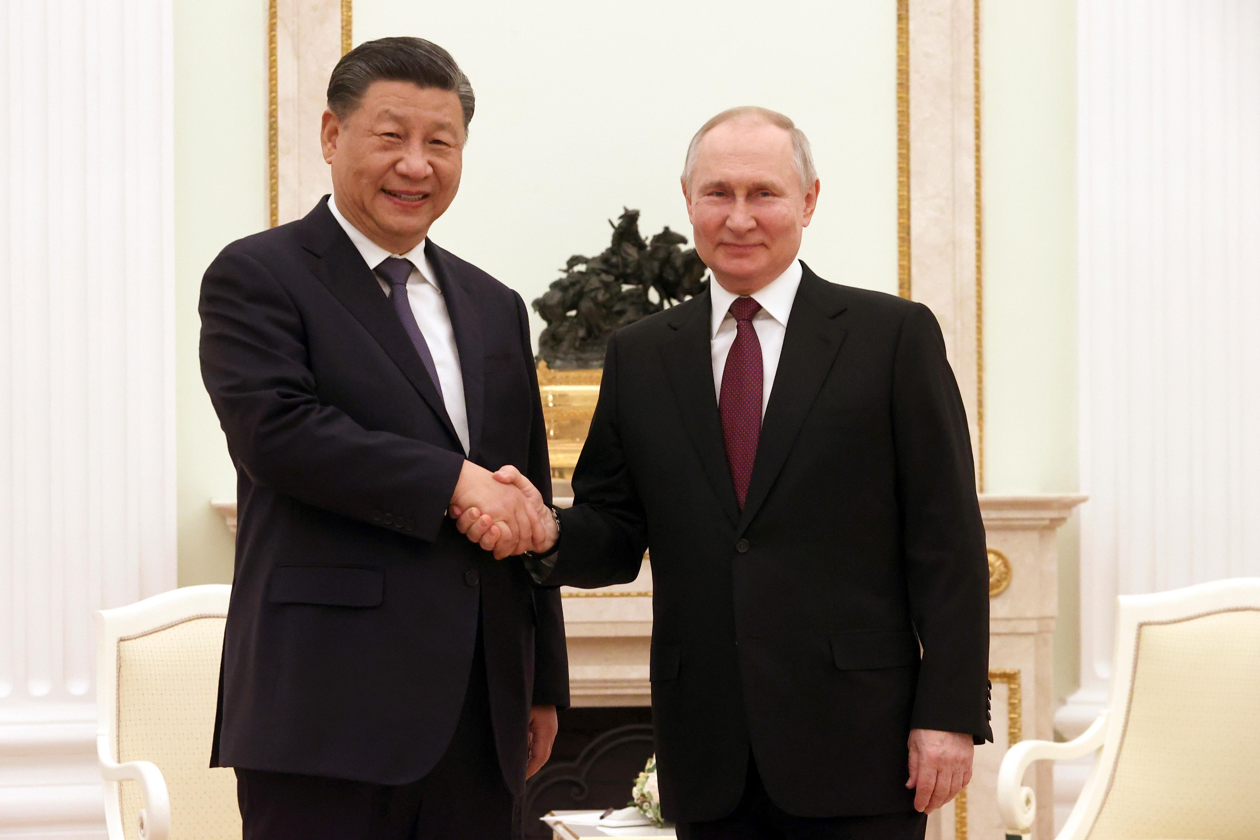 Chinese President Xi Jinping and Russian President Vladimir Putin shake hands as they pose for a photo.