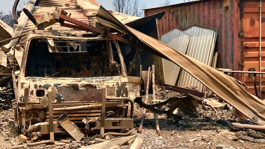 a tin roof collapsed over a truck which has been gutted by fire.