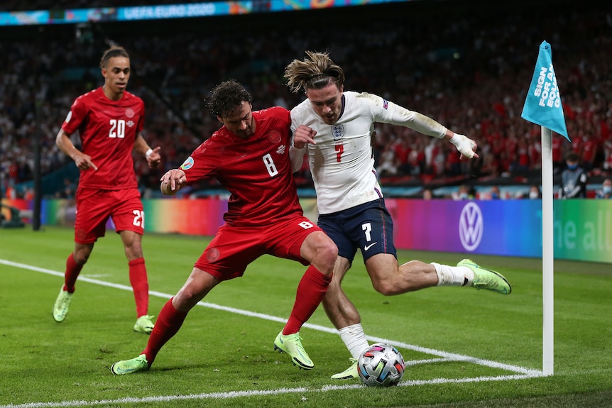 Jack Grealish's hair is flying as he tries to clear a ball in the corner. Thomas Delaney moves in to tackle