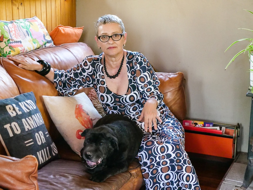 A woman sits on a couch with her dog