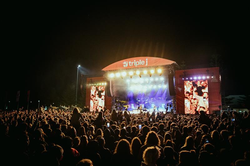 Crowd shot standing in-front of a triple j branded stage at a previous One Night Stand event. 